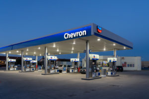 TWO CARS CAN BE SEEN AT A CHEVRON GAS STATION AT NIGHT.