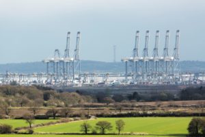 A ROW OF SHIPPING CRANES STANDS AT THE EDGE OF A WATERWAY