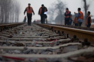 RAIL WORKERS WALK ALONG TRAIN TRACKS IN HIGH VISIBILITY VESTS