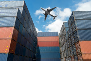 A GROUND VIEW OF AN AIRPLANE FLYING OVER MANY BLUE AND ORANGE SHIPPING CONTAINERS.