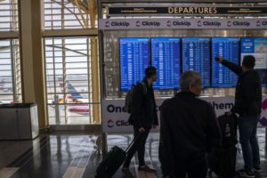 AIR PASSENGERS GESTURE AT A FLIGHT DEPARTURES SCREEN