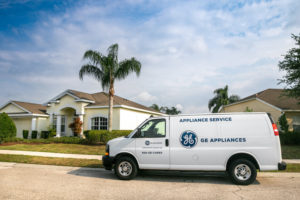 A GE APPLIANCES LABELED VAN SITS PARKED OUTSIDE OF A HOUSE. THE HOUSE HAS PALM TREE IN FRONT OF IT.