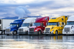Five brightly-colored semi-truck tractors are lined up side-by-side in a parking lot. Photo: iStock.com/vitpho