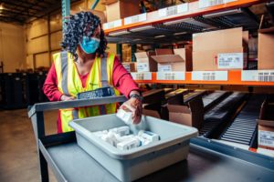 A WORKER PUSHES A CART FILLED WITH PRODUCT THROUGH A WAREHOUSE