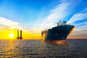 AN OIL TANKER MOVES AWAY FROM AN OIL PLATFORM AT SUNSET.