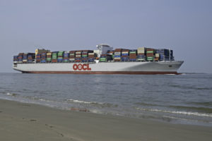 A LARGE CONTAINER SHIP TRAVELING NEAR THE SHORE HAS AN OOCL LOGO ON THE SIDE OF IT.
