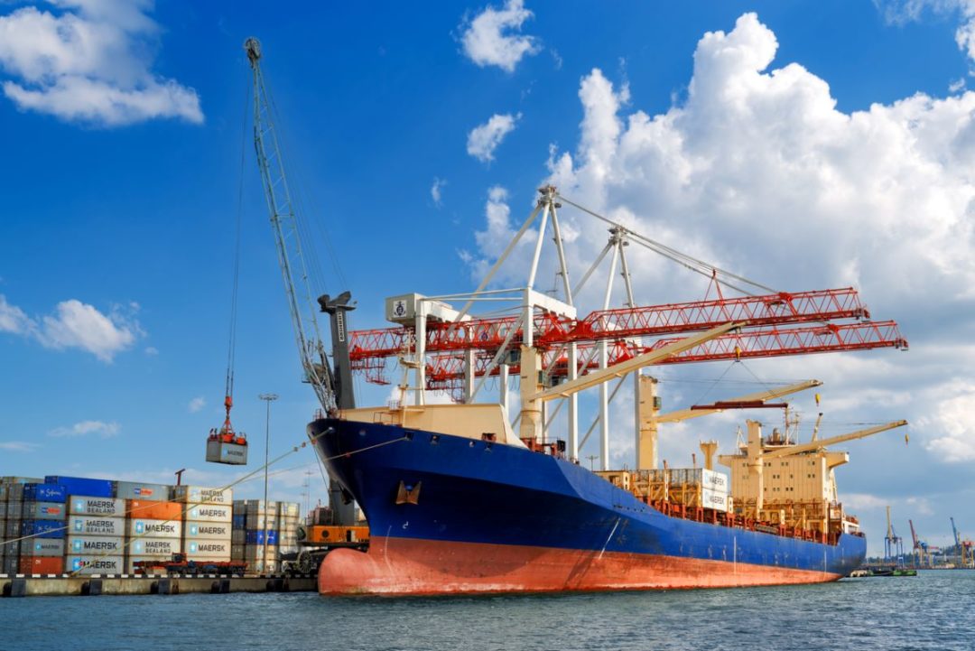 A CONTAINERSHIP UNLOADS A CONTAINER AT A DOCK UNDER A BRIGHT BLUE SKY